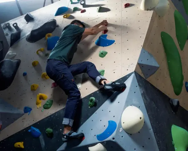 Mann klettert an einer bunten Kletterwand, die aussieht, als ob sie jemand selber bauen könnte.