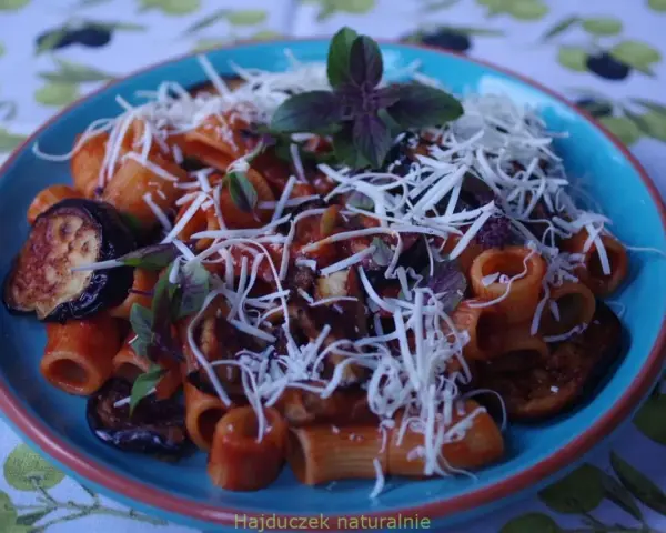 Pyszne danie pasta alla norma z makaronem rigatoni, bakłażanem w sosie pomidorowym i posypane startym serem.