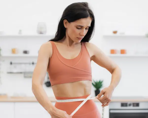 Kobieta w sportowym stroju mierzy talię, ciesząc się efektami diety low carb.