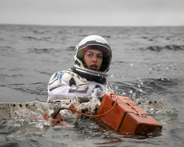 Astronautka w skafandrze z filmu Interstellar 2 w wodzie, z pomarańczowym urządzeniem.
