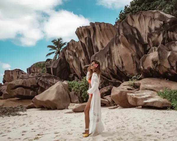 Kobieta w białej narzutce na plaży Anse Source d'Argent, Seszele. Co zobaczyć? Monumentalne granitowe skały i turkusowe niebo.