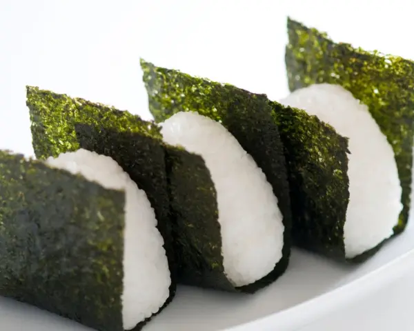 Trzy ryżowe onigiri owinięte w arkusze nori. Prosty sposób, jak przygotować nori do sushi, by nadać mu chrupkość i smak.