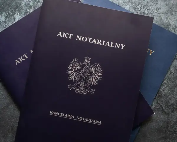 Stos dokumentów, na wierzchu ciemnogranatowy akt notarialny z godłem Polski.