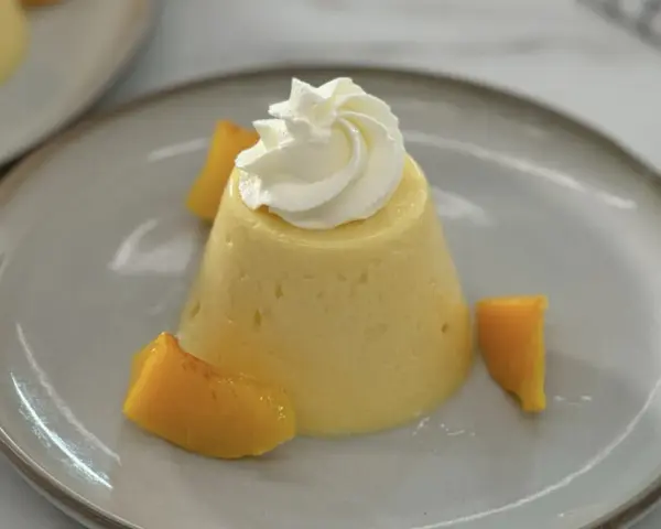 Postre de melocotón en almíbar con crema batida y trozos de melocotón.