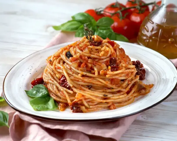 Un piatto di spaghetti conditi con un sugo rosso ricco di pomodori secchi, basilico fresco e un filo d'olio d'oliva.