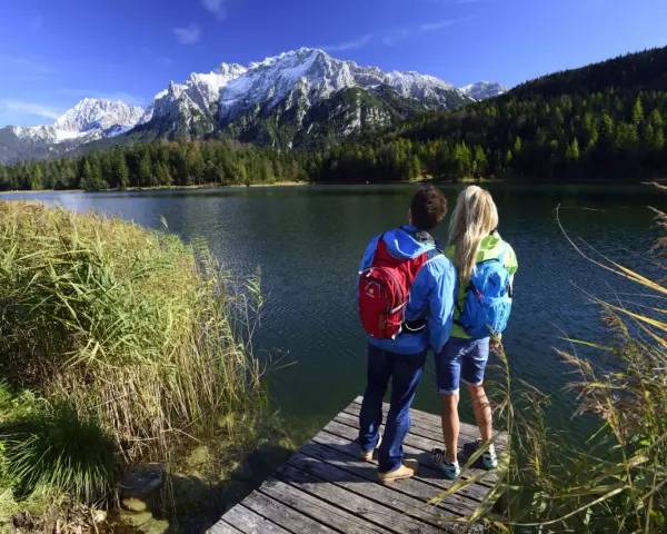Ein Paar genießt die Aussicht auf die Berge bei Garmisch-Partenkirchen. Sie stehen auf einem Steg am See, bereit zum Wandern.