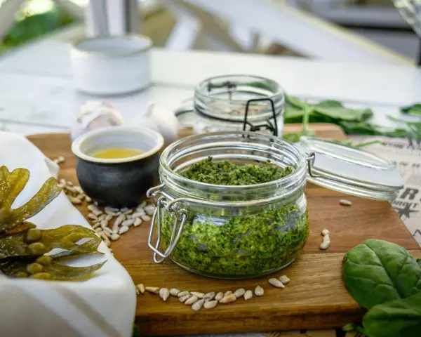 Frisches Pesto aus essbaren Algen der Nordsee, daneben Sonnenblumenkerne, Knoblauch und ein kleines Schälchen mit Öl.
