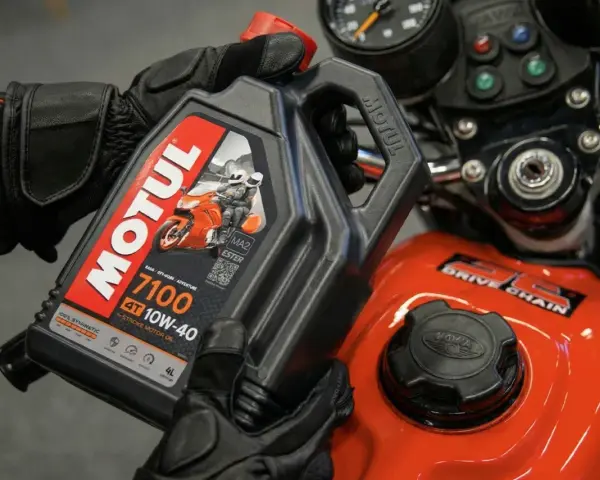 Ręce w rękawiczkach trzymają olej Motul 7100 10W-40. Pytanie: co ile wymieniać olej w motocyklu?