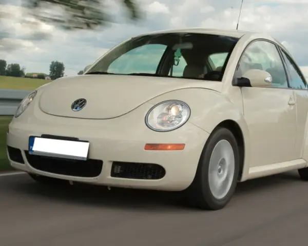 Jasny Volkswagen Beetle w ruchu na drodze, z rozmytym tłem.