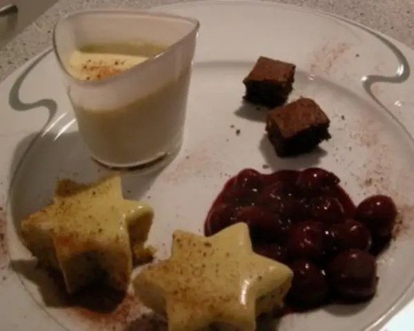 Sterne aus Zimtstern-Eis, garniert mit Kirschen und Brownies, serviert auf einem Teller.