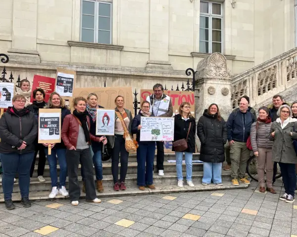 Un groupe de personnes manifeste devant un bâtiment, tenant des pancartes "Le Ministère de l'injustice".