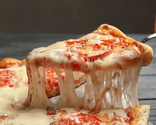 Rozciągający się, ciągnący ser na kawałku pizzy z pomidorami. Idealny przykład, jaki ser do pizzy wybrać, by uzyskać taki efekt.