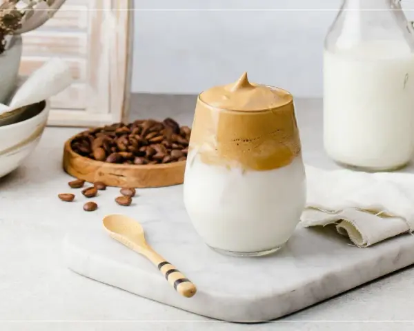 En krämig dalgona coffee med fluffigt skum, serverad med mjölk och kaffebönor.