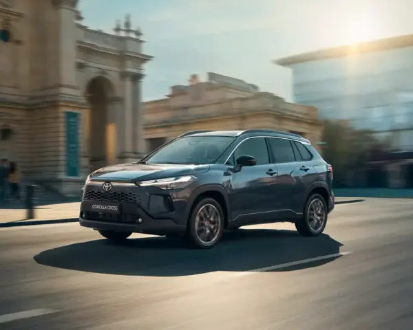 Ciemnoszary Toyota Corolla Cross Hybrid sunie ulicą miasta, odbijając światło słoneczne od nowoczesnych budynków.