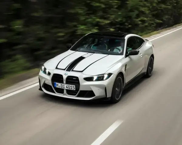 Białe BMW M4 z czarnymi pasami na masce pędzi po krętej drodze. Zastanawiasz się, ile kosztuje BMW M4?