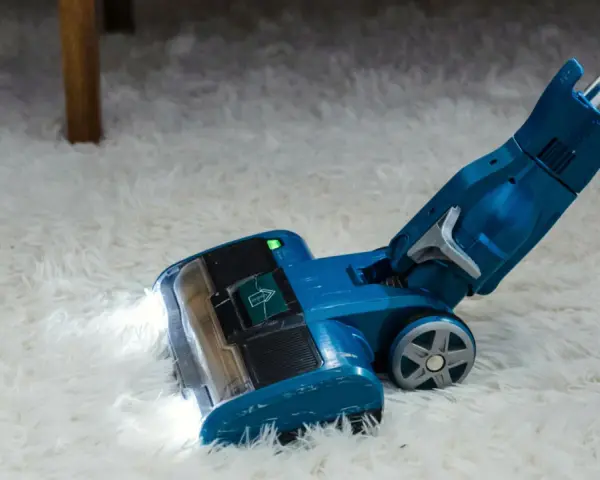 Blauer Staubsauger mit LED-Licht reinigt flauschigen Teppich. Die Leistung, wie viel Watt hat ein Staubsauger, ist entscheidend für die Saugkraft.