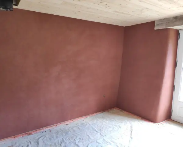 Un coin de pièce aux murs recouverts d'un enduit chaux sable ocre. Le sol est protégé par une bâche. Le plafond est en bois clair.
