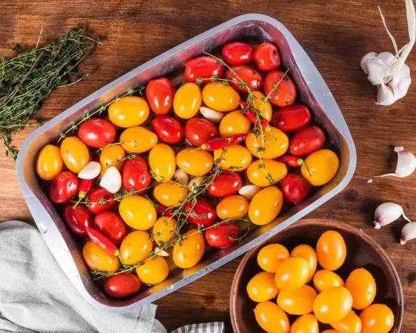 Pomodorini al forno rossi e gialli, aglio e peperoncino in una teglia, pronti per essere cotti.