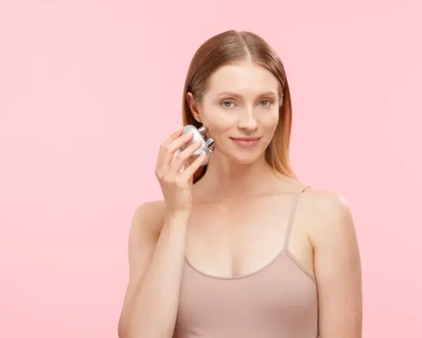 A woman demonstrates how to use a face massager on her cheek, showing a simple skincare routine.