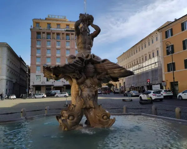Fontana del Tritone in Piazza Barberini, Roma, con edifici storici e traffico sulla via dei Cappuccini.