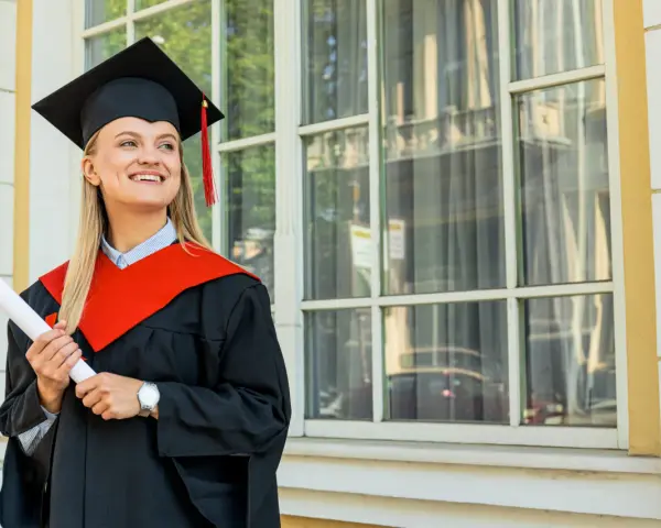Uśmiechnięta absolwentka z dyplomem, w todze i birecie, zastanawia się, co to studia MBA i jakie możliwości otwierają.
