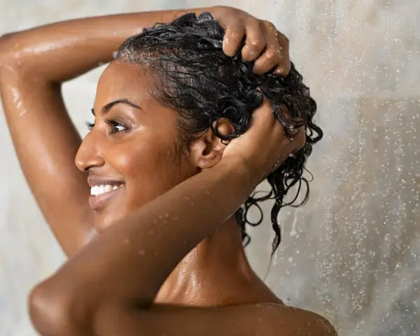Frau wäscht sich unter der Dusche die Haare. Sie fragt sich, wie oft Haare waschen am besten ist.