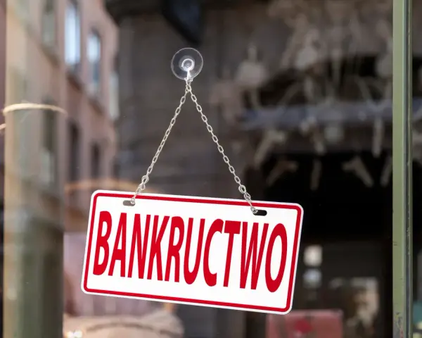Tabliczka "BANKRUCTWO" wisząca na łańcuszku na szybie.