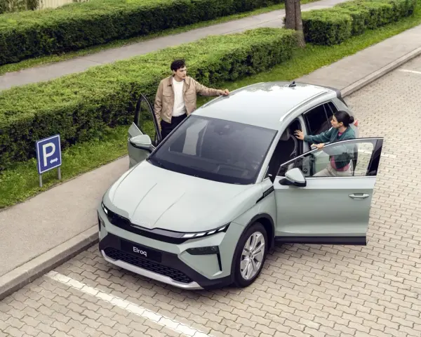 Jasnoszary elektryczny SUV Škoda Elroq z otwartymi drzwiami, obok którego stoją młoda kobieta i mężczyzna.