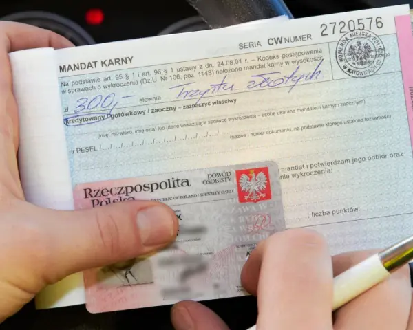 Ręka trzyma mandat karny na 300 zł i dowód osobisty. Ktoś wypełnia dokument, być może to mandat za parkowanie.
