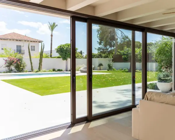 Amplias puertas correderas de cristal conectan el interior con un jardín con piscina, permitiendo una ventilación natural y la entrada de luz.