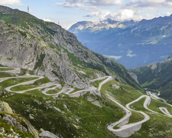 Strada tortuosa che sale sul passo Austria, circondata da montagne verdi e rocce imponenti.
