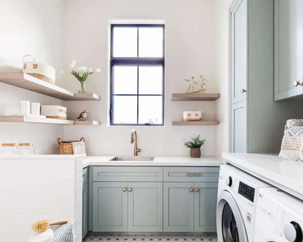Stylish laundry room with mint cabinets, floating shelves, and a sink. This organized space shows how to organize laundry room with baskets and jars.