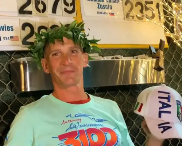 Vincitore con corona d'alloro, indossa una maglietta con scritto "3100" e un cappellino "ITALIA". Potrebbe essere un traguardo della ultramaratona più lunga del mondo.