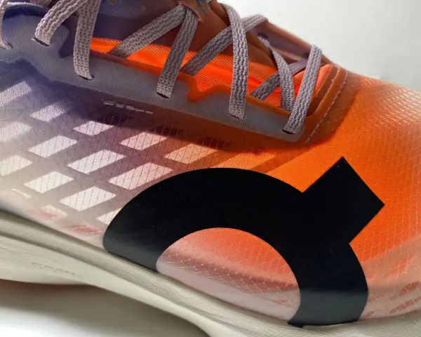 La tomaia di una scarpa da corsa arancione e viola con lacci grigi e un logo nero.