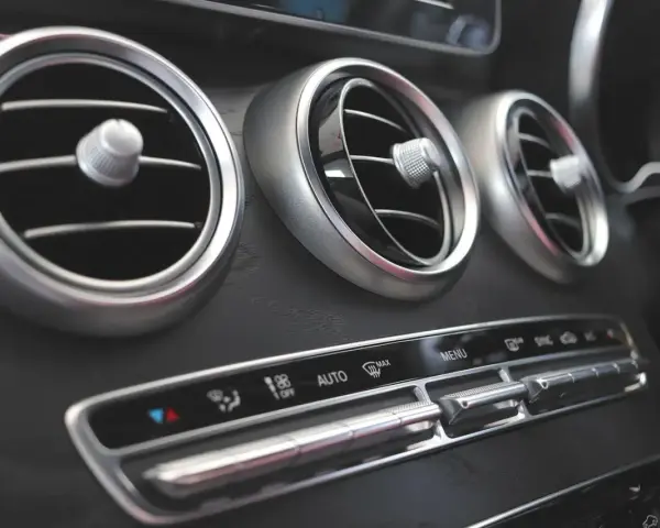Trzy okrągłe nawiewy wentylacji w samochodzie, z pokrętłami do regulacji. Poniżej panel sterowania klimatyzacją, z przyciskami AUTO i MAX. Czekam na bardzo gorące powietrze z nawiewu.