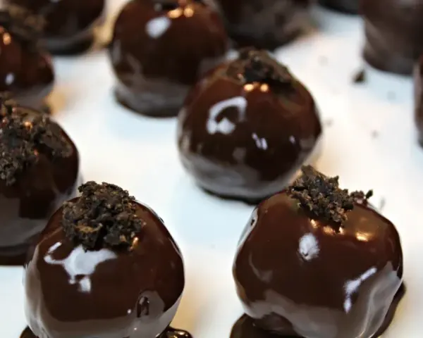 Deliziosi tartufini al cocco ricoperti di cioccolato fondente lucido, guarniti con briciole croccanti.