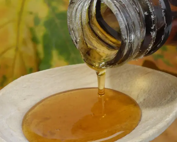 Ahornsirup tropft aus einer Flasche auf einen Holzlöffel. Die Frage, ob kann ahornsirup schlecht werden, beschäftigt viele.