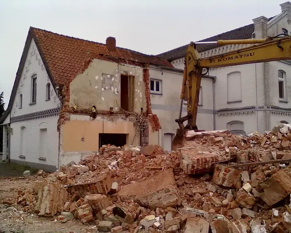 Rozbiórka budynku w granicy działki. Koparka Komatsu pracuje przy gruzach.
