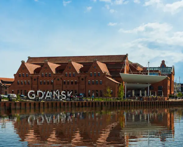 Gdańsk zwiedzanie: ceglane kamieniczki nad Motławą, wielki napis "GDAŃSK" i odbicie w wodzie.