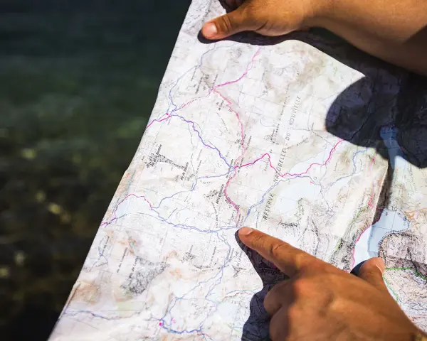 Une main pointe un itinéraire sur une carte topo détaillée, près d'une étendue d'eau.