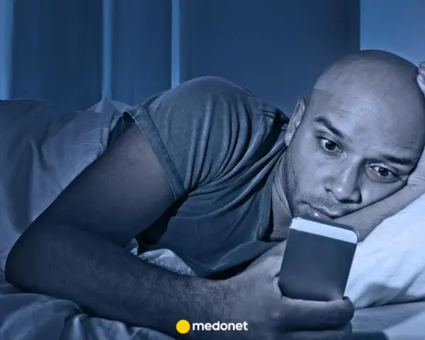 Mężczyzna leży w łóżku, wpatrując się w telefon. Czy to już obsesja?