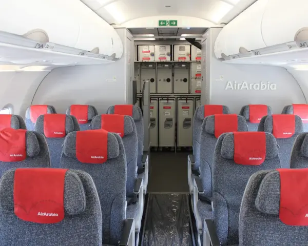 Wnętrze samolotu Air Arabia z rzędami szarych siedzeń i czerwonymi zagłówkami. W tle widać wózki pokładowe. Dobre **air arabia opinie** potwierdzają komfort podróży.