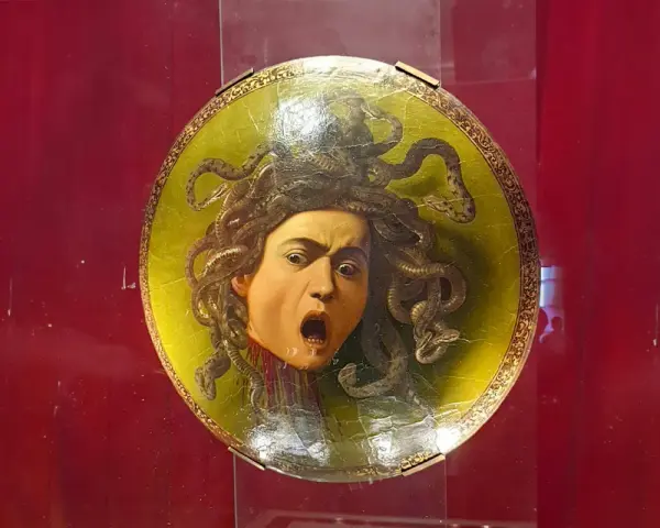 Przerażająca Meduza Caravaggia na okrągłej tarczy, z wężami zamiast włosów i wykrzywioną w krzyku twarzą.