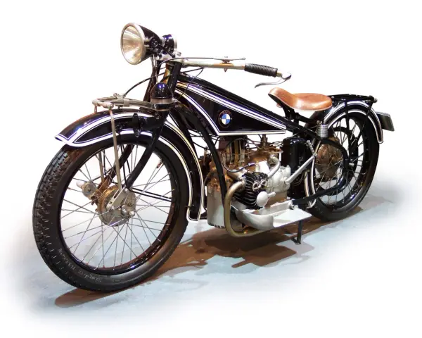 Klasyczny motocykl BMW z lat 20. XX wieku, czarny z białymi pasami, z brązowym siodłem. Ikona historii BMW.
