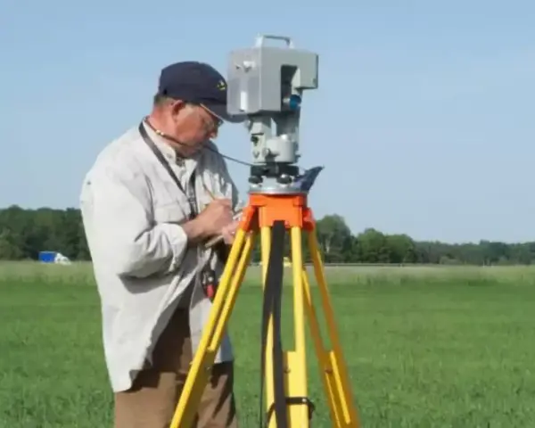 Geodeta precyzyjnie wyznacza granice działki za pomocą tachimetru na statywie, pracując na zielonym polu.