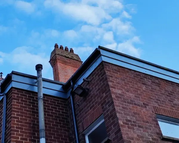 Vue d'une maison en briques rouges avec une cheminée traditionnelle et un conduit de poêle à bois sortie ventouse en façade. Ciel bleu avec quelques nuages.