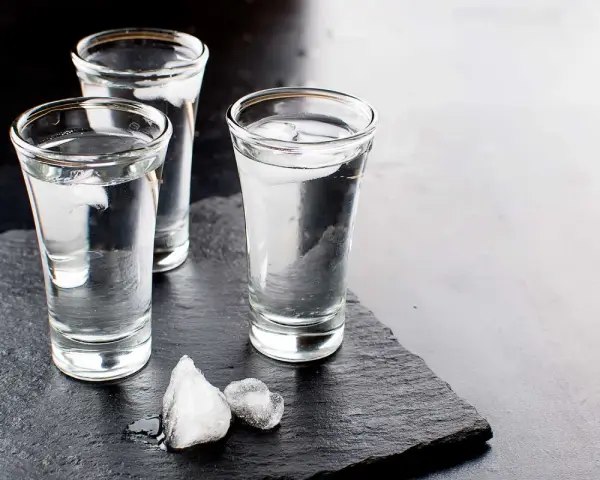 Drei Gläser Wodka mit Eiswürfeln auf dunklem Stein. Wodka wird aus Getreide oder Kartoffeln hergestellt.
