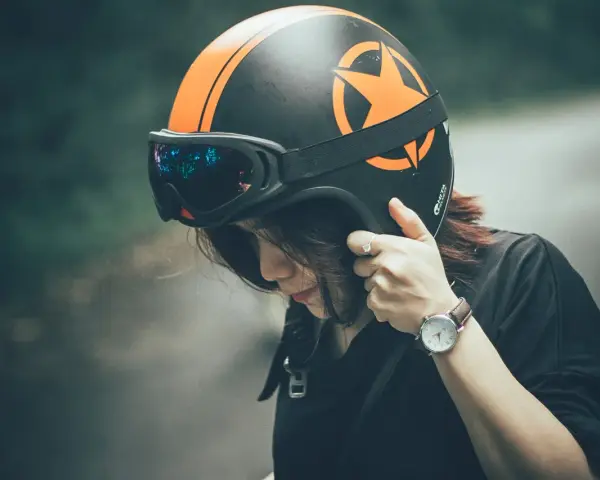 Ragazza con casco moto nero e arancione, occhiali vintage. Guida sicura: come scegliere casco moto.