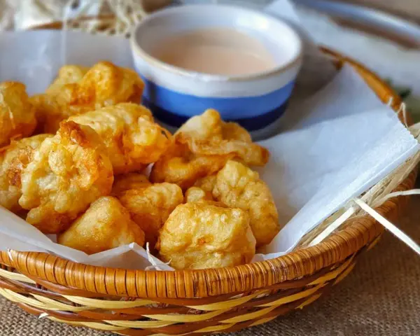 Cesta de mimbre con crujientes fritos de pixin, acompañados de una cremosa salsa rosa. ¡Un bocado delicioso!
