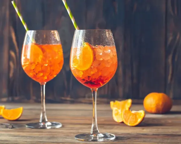 Dwa orzeźwiające drinki z sokiem pomarańczowym, lodem i plasterkiem pomarańczy, ozdobione słomkami.